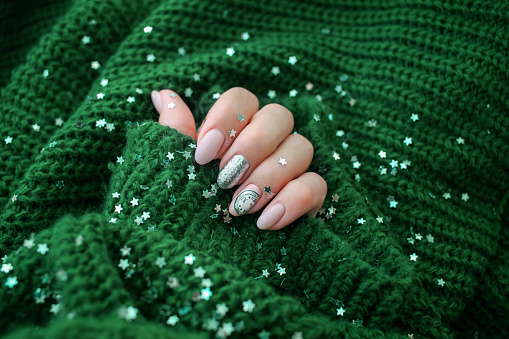 Beautiful female hand in a green sweater with Christmas nail design. Nail design, manicure with chimes pattern.  Shellac, gel polish.