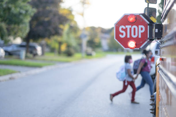 A STOP sign is out by the school bus and children can be seeing crossing the road in front of the school bus.