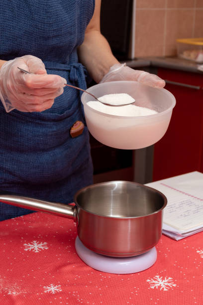 The pastry chef uses a spoon to pour the sugar into the pan to make the syrup. Selective focus. stock photo