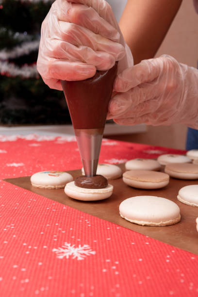 from the pastry bag, squeeze the filling into half of the macaroon. the process of making christmas dessert. close up. selective focus. - fragility organization chef cake imagens e fotografias de stock