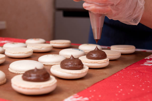 applying chocolate filling to macaroons from a pastry bag. the process of making christmas dessert. close up. selective focus. - fragility organization chef cake imagens e fotografias de stock