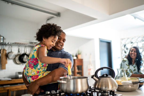 Girl in father's arms helping him cooking at home Girl in father's arms helping him cooking burner stove top stock pictures, royalty-free photos & images
