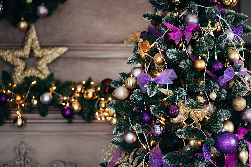 Christmas decorations in violet and golden color on the branches of fir. Decorated Christmas tree on blurred, sparkling and fairy background. New year concept.