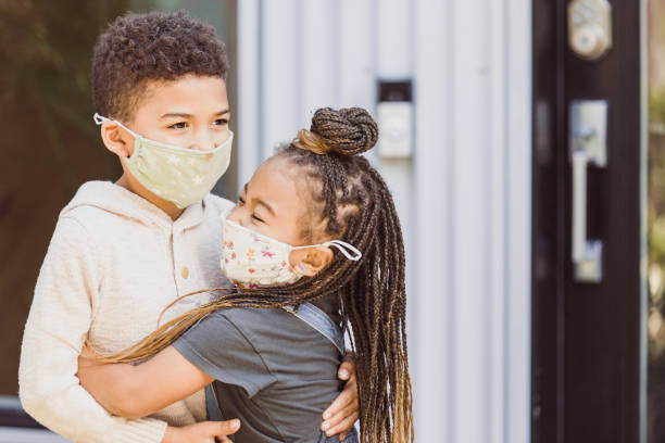 istock Sister enthusiastically hugs brother; both wear protective masks 1291284648