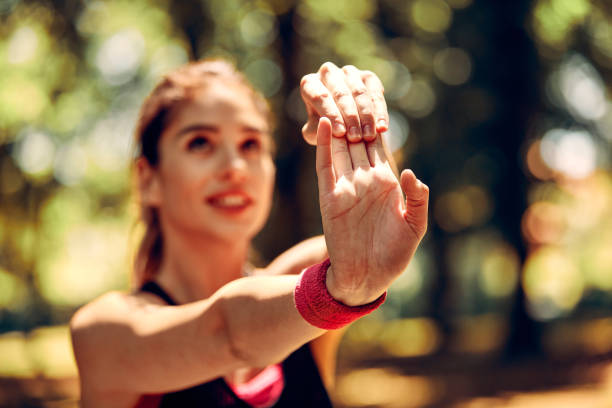 istock Young fit smiling female runner in shape stretching her hand and doing warmup exercises before running in nature. Selective focus on hand. 1291286652
