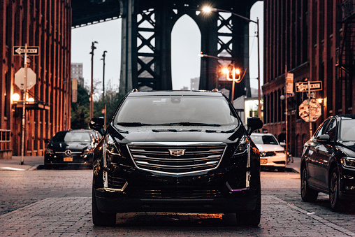 Brooklyn. New York, USA - May 3, 2019: A 2018 Cadillac XT5 is parked along the street of Dumbo district in Brooklyn with the Manhattan Bridge in the background . XT5 is the new suv by Cadillac, one of the most famous automotive brand in United States. Pic as been taken at night after the rain.