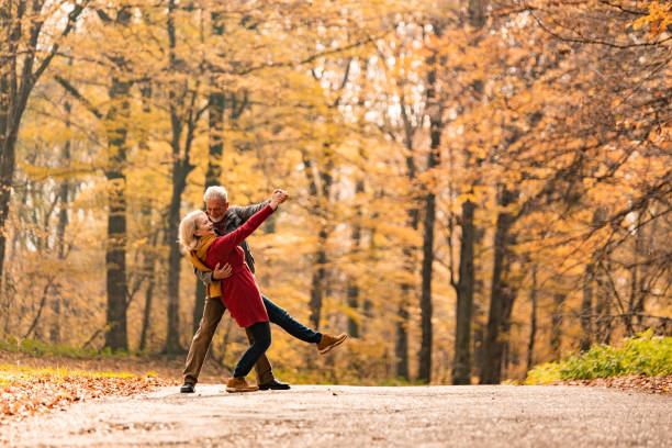 Playful romantic senior couple dancing on a forest road.