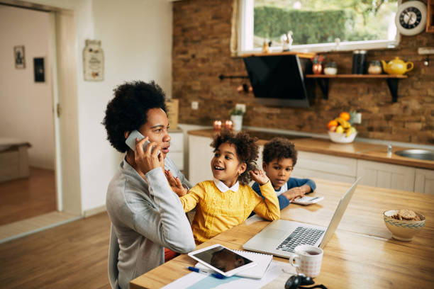 istock Black working mother talking on the phone while being at home with her children. 1291294253