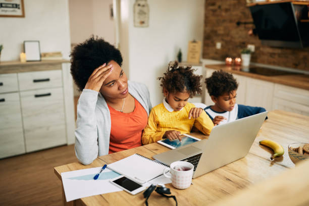 African American single mother feeling stressed out while working at home. Pensive African American mother with two children feeling distressed about working from home. banging your head against a wall photos stock pictures, royalty-free photos & images