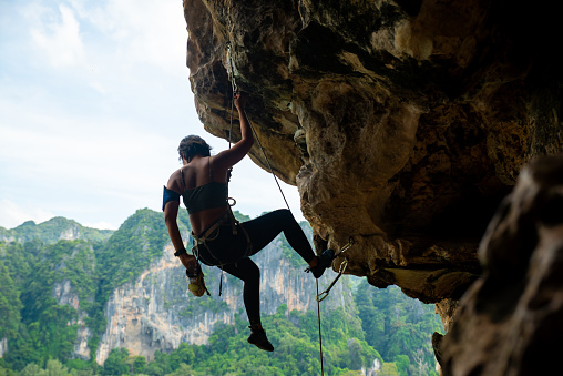 Asian woman climbing on rocky mountain at tropical island in summer.