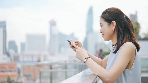 istock Asia happy smile cheerful asian working women relaxing using smartphone relaxtion afterwork at sunset bangkok background 1291312976