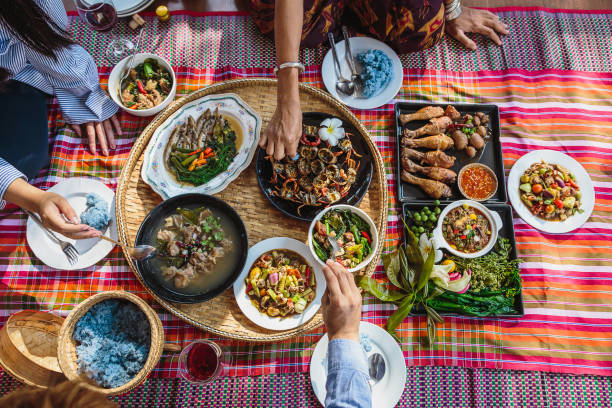 กลุ่มคนเอเชียครอบครัวเพลิดเพลินกับการเฉลิมฉลองอาหารค่ําอาหารไทยในขณะที่นั่งอยู่บนเสื่� - อาหารไทย ภาพสต็อก ภาพถ่ายและรูปภาพปลอดค่าลิขสิทธิ์