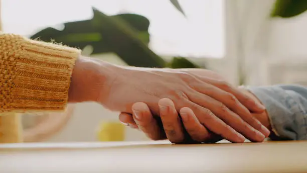 Shot of an unrecognisable couple sitting at a table and holding hands at home