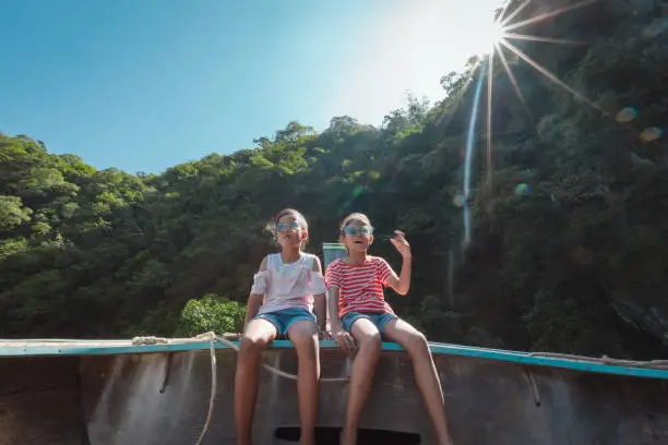 Two asian child girls sitting on the head of wooden longtail boat travel on the sea go to the amazing island and lagoon and enjoying with beautiful nature together with family.
