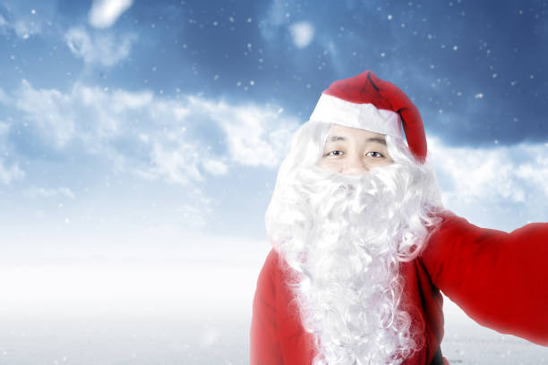 istock Asian man in Santa costume taking a selfie with a snowfall background 1291322177
