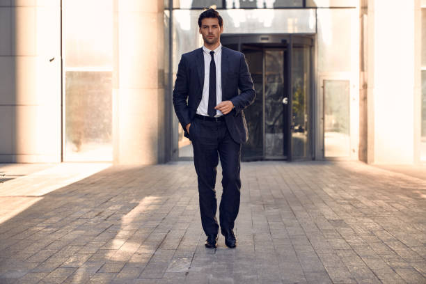 istock Young and successful. Handsome young businessman adjusting his jacket and looking away while walking outdoors with office building in the background 1291322271