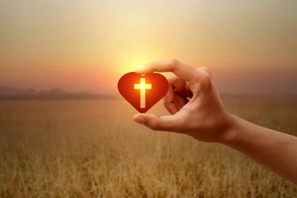 mano humana sosteniendo un corazón rojo con una cruz cristiana - god light sunbeam jesus christ fotografías e imágenes de stock
