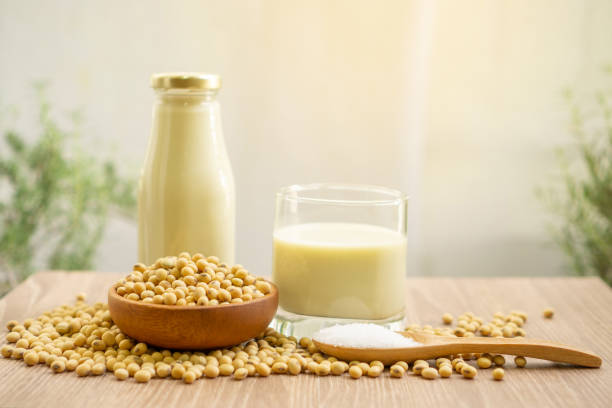 Fresh soybean seeds in brown wooden bowl with sugar in a spoon, a bottle and a glass of soy milk on the table,  under sunlight morning blurred background, delicious healthy drinking for breakfast stock photo