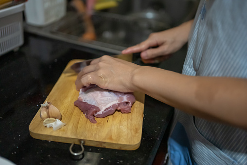 Female hand with cutting a beef roast with a large knife in a kitchen