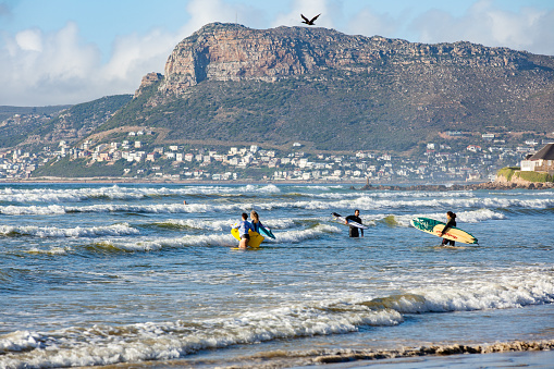 Cape Town, South Africa - December 10, 2020: Surfers enter the waves at South Africa's popular surfing spot of Muizenberg in Cape Town. The beach is still open to the public although the South African government has closed many beaches over the December/January holiday season to prevent crowding and the risk of Covid-19 infection. It is the height of summer in the southern hemisphere.