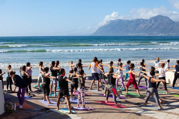 people doing group yoga in the early morning at muizenberg beach, cape town - cape town beach crowd people imagens e fotografias de stock