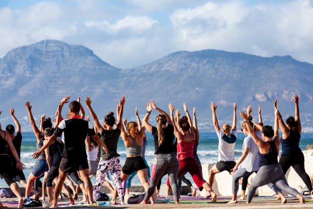 people doing group yoga in the early morning at muizenberg beach, cape town - cape town beach crowd people imagens e fotografias de stock