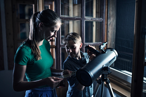 Brother and sister are using the astronomy telescope to observe the moon and the stars. The girl is using sky map.
Nikon D850