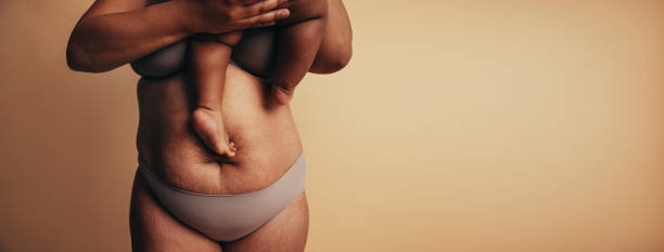 Postpartum belly with stretch marks Midsection of mother carrying child while standing against brown background. Postpartum belly with stretch marks. postpartum depression stock pictures, royalty-free photos & images