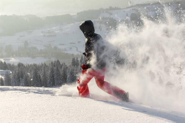 happy man mit kapuze läuft im tief schneebedeckten schnee mit schneeschuhen. schnee spritzt und spritzt. - winter snowshoeing running snowshoe stock-fotos und bilder