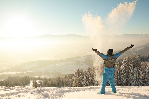 Happy Man standing in deep snow throwing snow into sunrise sunlight. Beautiful Winter Mountains Landscape. Allgäu, Bavaria, Alps, Germany.