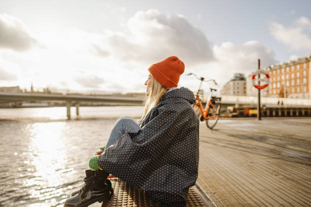Enjoying the view Photo of a young woman sitting on the dock; enjoying the view and the calmness of the sea while spending time outdoors, on a cold winter day. nyhavn stock pictures, royalty-free photos & images