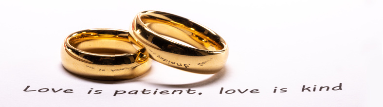 Two golden wedding rings on Holy bible book phrase close up, love is patient, love is kind