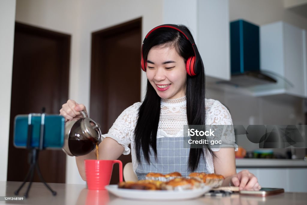 Young Asian woman having tea break with homemade pastries at domestic kitchen Young Asian woman having tea break with homemade pastries at domestic kitchen. She taking a short break from work and learning online bakery and working from home. 5G & Wireless Technology, Home Hobbies & Self Development, Healthier, Longer and Better Lives Concepts. 25-29 Years Stock Photo