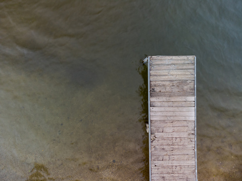 Aerial top down drone shot of wooden pier for swimmers and boats leading into swimming lake of local recreation area