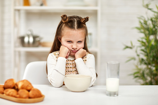 the child does not want to have breakfast. little girl looks at the cereal with the milk with disgust