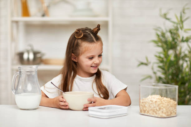 menina tomando café da manhã: cereal com o leite na cozinha. - healthy eating snack child domestic kitchen - fotografias e filmes do acervo