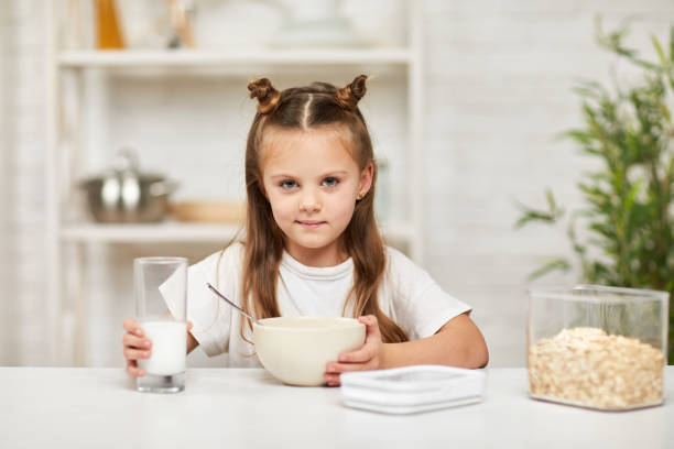 menina tomando café da manhã: cereal com o leite na cozinha. - healthy eating snack child domestic kitchen - fotografias e filmes do acervo