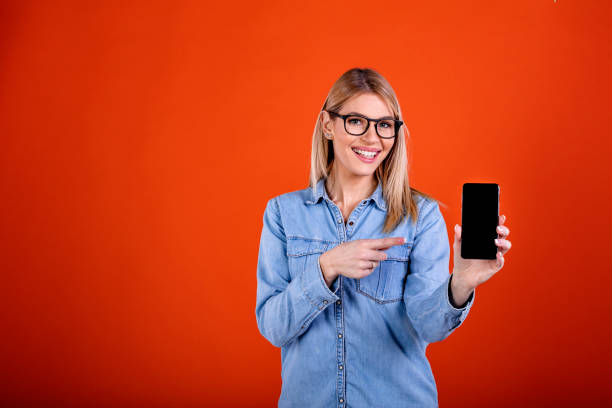 istock Cute woman standing, holding and pointing at mobile display. 1291352654