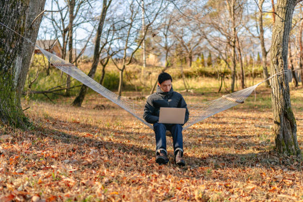 istock Young man sitting on hammock and working remotely on laptop in nature 1291357774