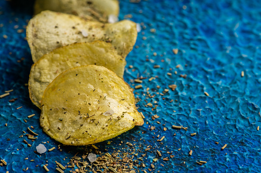 Homemade crispy potato chips with italian spices on the blue rustic background. Selective focus.