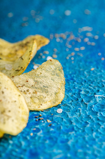Homemade crispy potato chips with italian spices on the blue rustic background. Selective focus.