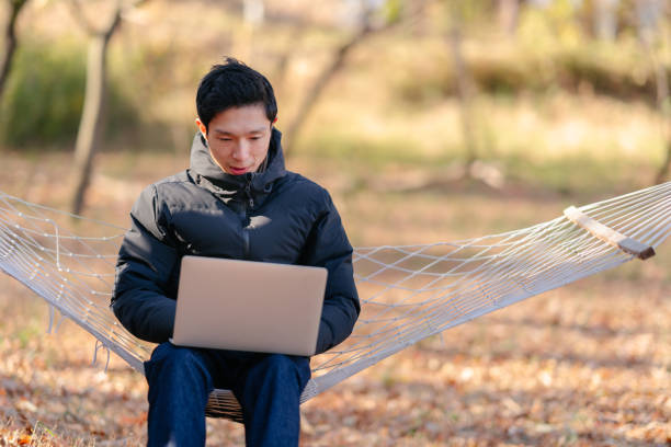 Young man sitting on hammock and working remotely on laptop in nature
