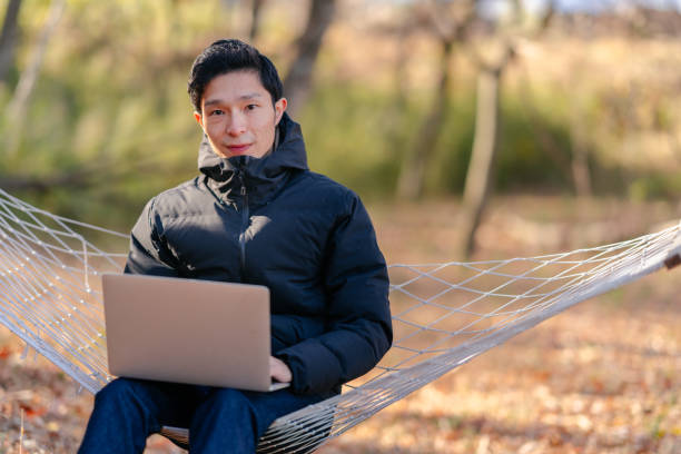 istock Young man sitting on hammock and working remotely on laptop in nature 1291358277
