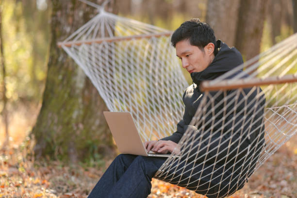 istock Young man sitting on hammock and working remotely on laptop in nature 1291358797