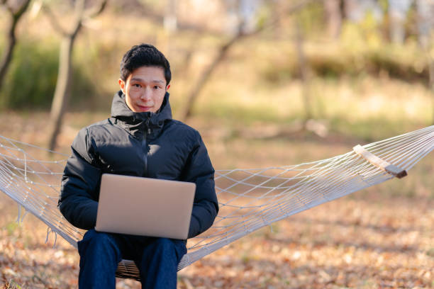 istock Young man sitting on hammock and working remotely on laptop in nature 1291358987