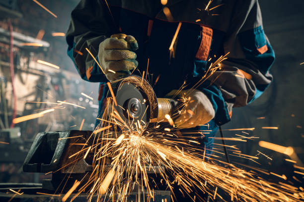 istock Locksmith in special clothes and goggles works in production. Metal processing with angle grinder. Sparks in metalworking 1291359292