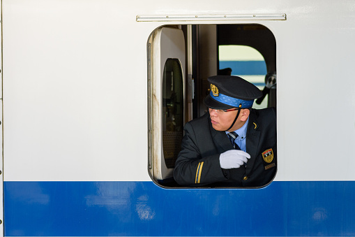 Osaka / Japan - December 20, 2017: Japanese train driver looking through the window and checking if all the passengers have boarded the shinkansen bullet train at Shin-Osaka station