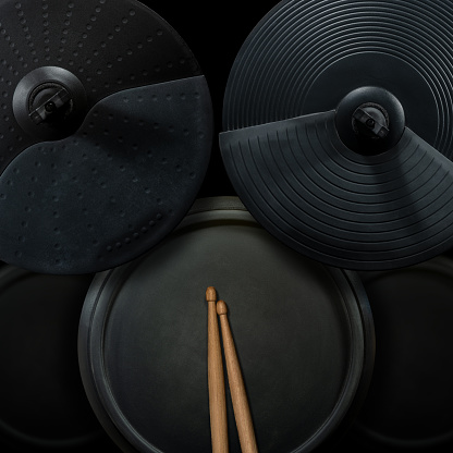 Top view of a black electronic drum kit with cymbals and drums and a pair of wooden drumsticks, on a black background. Percussion instrument concept.