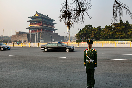 Beijing, China - November 19, 2019: Guard soldier or Guard Officer on a street in Beijing near the forbidden city,  guards the passing of a government vehicle. The Zhengyangmen gate in the background