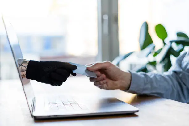 Digital illustration of hand reaching out from a laptop screen to steal a credit card. This illustrates the cyber crime of identity theft and credit card fraud.